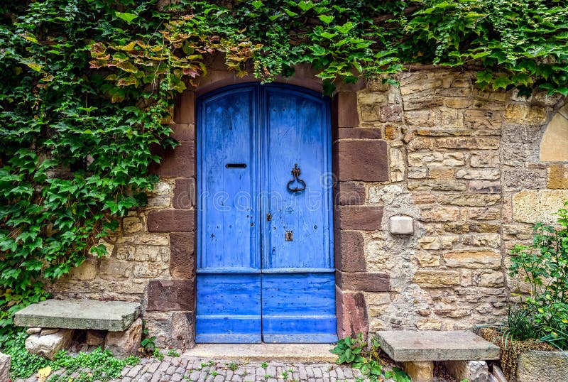 A blue and worn door with green ivy above on the stone walls of a small town in French countryside. A blue and worn door with green ivy above on the stone walls of a small town in French countryside