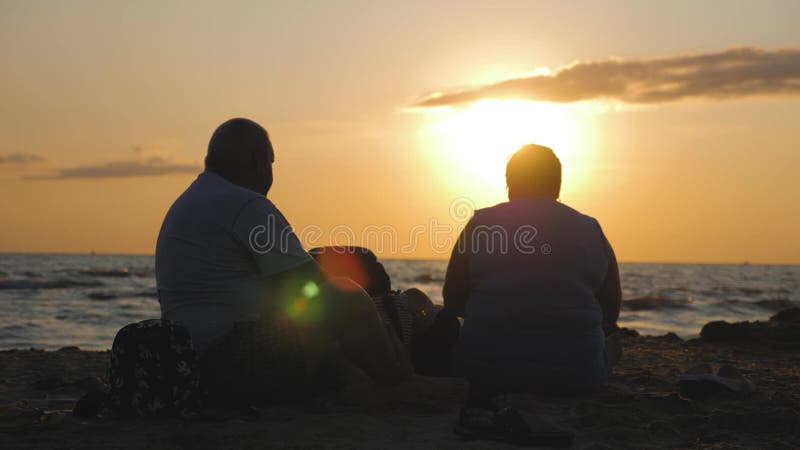 Une silhouette d'un couple âgé, assise sur la plage au coucher du soleil, jouissant d'une belle vue sur la mer et la banque de vidéos
