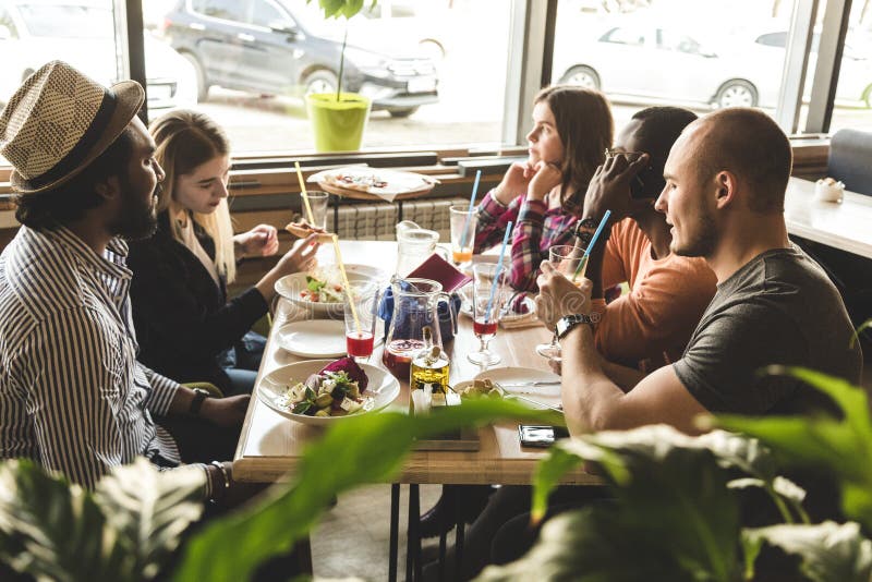 Une soci?t? des jeunes multiculturels dans un caf? mangeant de la pizza, cocktails potables, ayant l'amusement images stock Une soci?t? des jeunes multiculturels dans un caf? mangeant de la pizza, cocktails potables, ayant l'amusement images stock