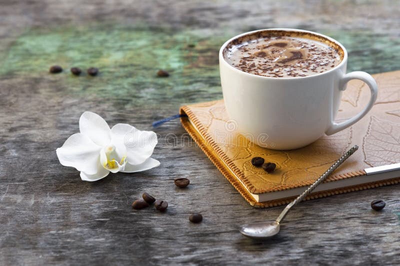 Une tasse de café chaud et une orchidée fleurissent avec un journal intime sur un fond en bois Boisson traditionnelle de dos en b photographie stock libre de droits Une tasse de café chaud et une orchidée fleurissent avec un journal intime sur un fond en bois Boisson traditionnelle de dos en b photographie stock libre de droits