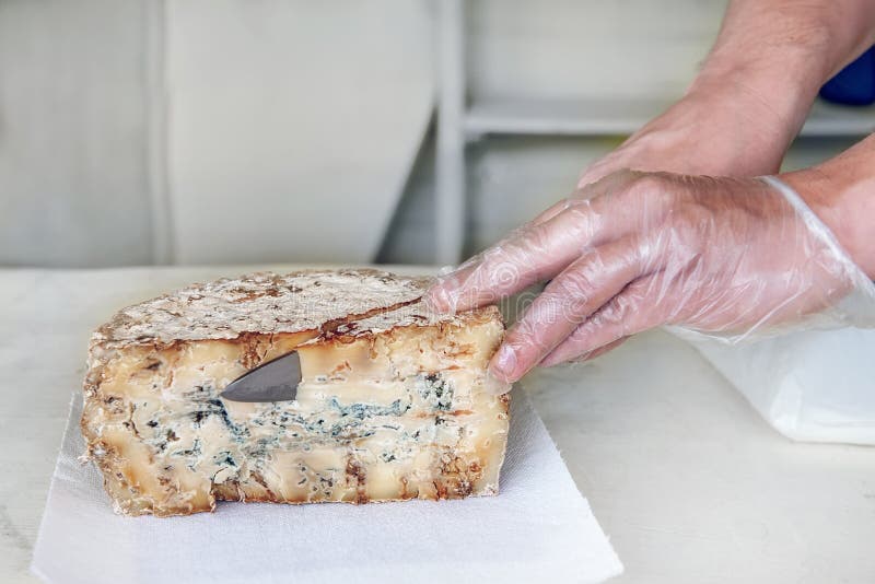 Une tranche de fromage âgé bleu de stilton d'épicerie fine sur une table blanche Le vendeur coupe un morceau de la tête de fromag photographie stock libre de droits Une tranche de fromage âgé bleu de stilton d'épicerie fine sur une table blanche Le vendeur coupe un morceau de la tête de fromag photographie stock libre de droits