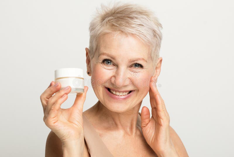 Une vieille dame charmante avec une courte coiffure sourit et tient un bocal de crème dans les mains. routine beauté. photos stock