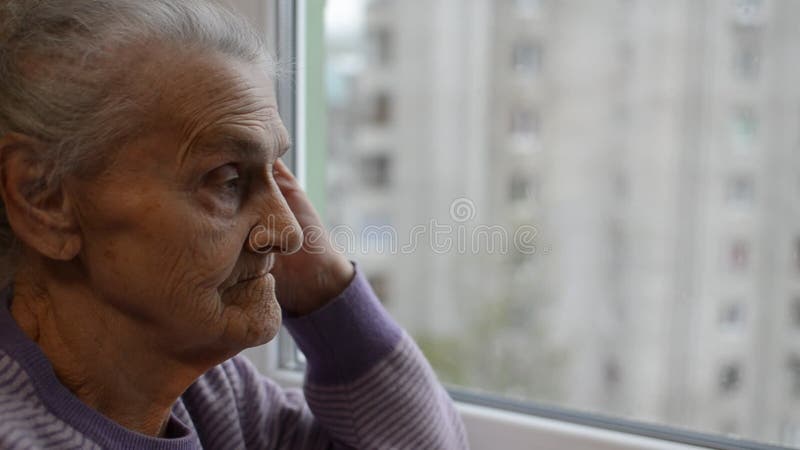 Une vieille femme regarde par la fenêtre et est triste banque de vidéos