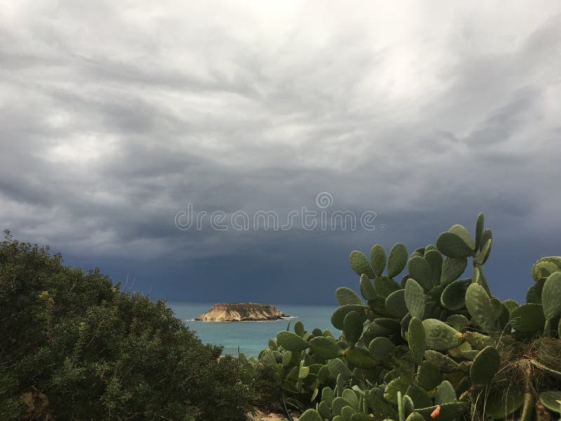 Une vue de la mer et de l'île tropicale avec le cactus dans le premier plan avant la tempête avec les nuages bleu-foncé approc photos stock Une vue de la mer et de l'île tropicale avec le cactus dans le premier plan avant la tempête avec les nuages bleu-foncé approc photos stock