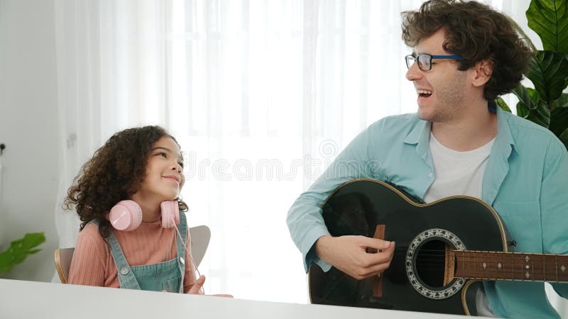 Une écolière heureuse debout et dansant pendant que papa intelligent joue de la guitare. pédagogie. photos libres de droits