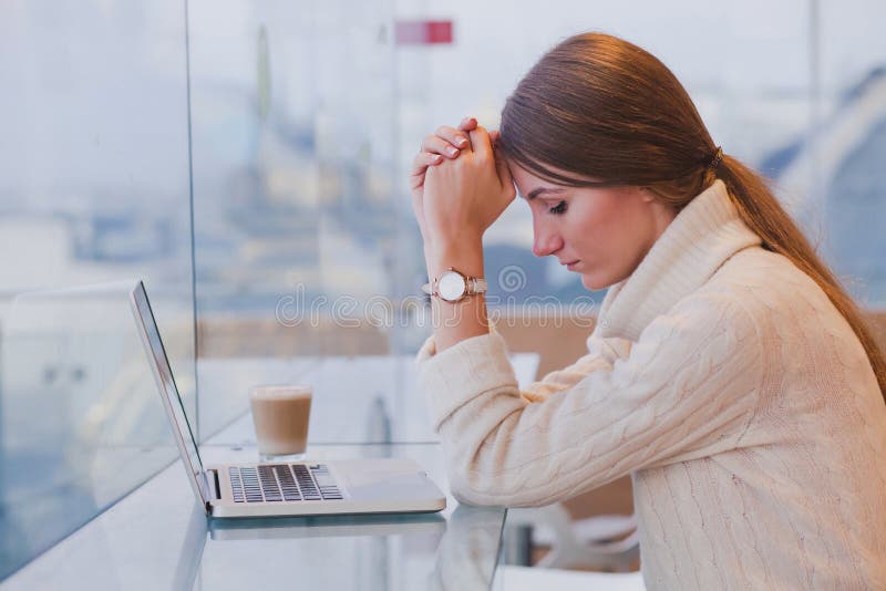 Nezaměstnanost koncept, problém, smutná, unavená žena v přední části notebooku v moderní světlý interiér kavárny.