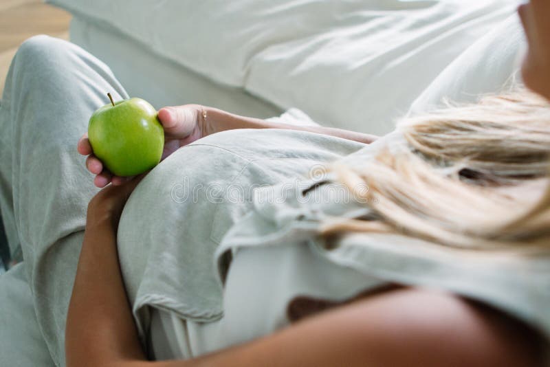 Unerkennbar schöne schwangere junge Frau, die zu Hause im Wohnzimmer einen Apfel isst stockfotos Unerkennbar schöne schwangere junge Frau, die zu Hause im Wohnzimmer einen Apfel isst stockfotos