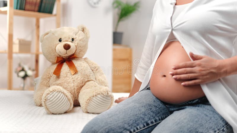 Unerkennbare schwangere Frau, die mit der Hand die Bauchdecke streichelt und liebevoll im kindischen Zimmer wartet, Spielzeug
