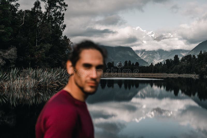 Unfocused disheveled caucasian guy with beard calm and relaxed looking at camera at lonely cold water lake among forest royalty free stock images