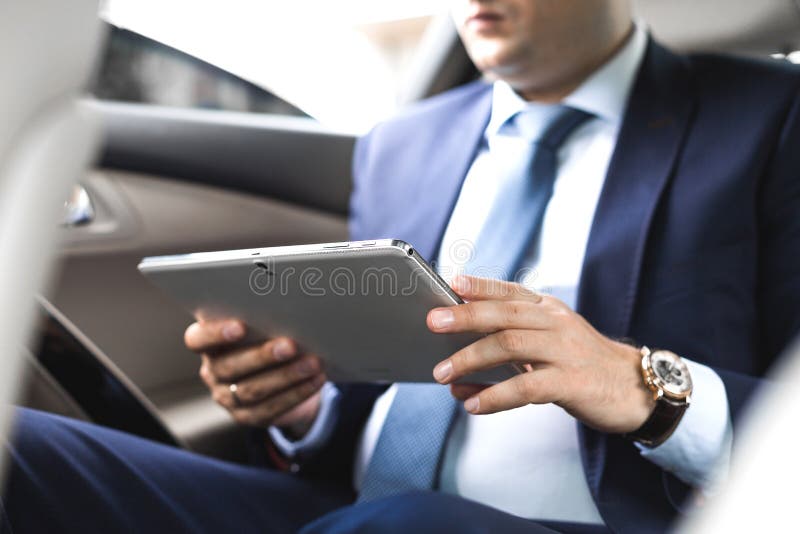 Ung aff?rsman som anv?nder minnestavlaPC, medan sitta p? baks?tet av en bil Caucasian manlig affärsledare vid en taxi och se royaltyfri foto Ung aff?rsman som anv?nder minnestavlaPC, medan sitta p? baks?tet av en bil Caucasian manlig affärsledare vid en taxi och se royaltyfri foto