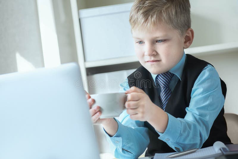 Ung affärsman som arbetar på en bärbar dator med vit kopp kaffe eller varmt te Lustig liten chef på kontoret fotografering för bildbyråer