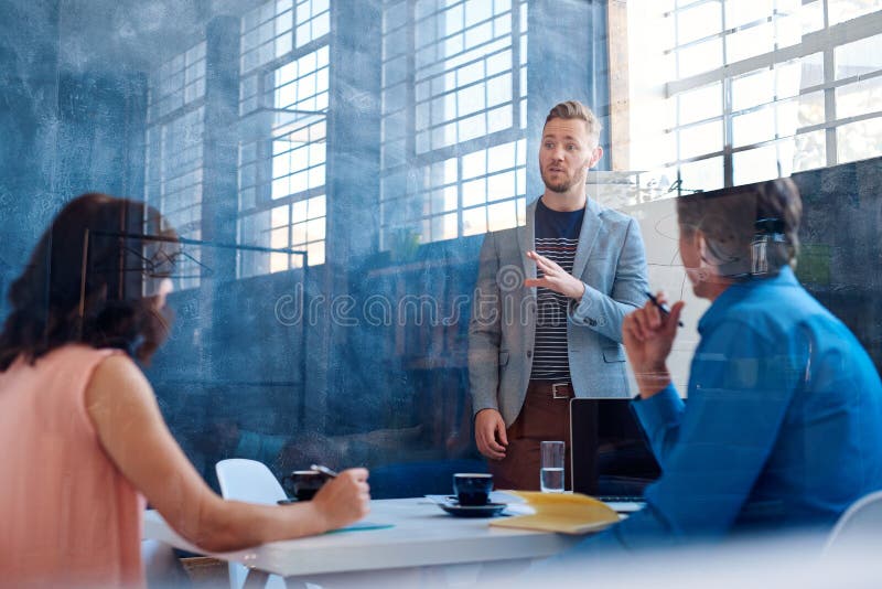 Ung affärsman som förklarar idéer till coworkers inom av ett kontor royaltyfria foton Ung affärsman som förklarar idéer till coworkers inom av ett kontor royaltyfria foton