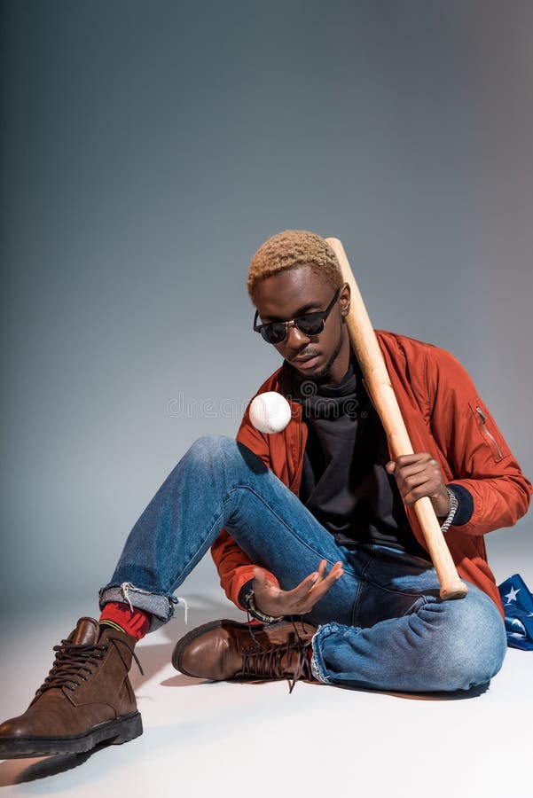 ung afrikansk amerikanman som sitter och rymmer baseballslagträet med bollen fotografering för bildbyråer ung afrikansk amerikanman som sitter och rymmer baseballslagträet med bollen fotografering för bildbyråer