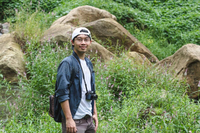 Ung asiatisk affärsföretagman som ser kameran med bakgrund för naturgräsplanberg Lopplivsstil och avkopplingbegrepp royaltyfria foton Ung asiatisk affärsföretagman som ser kameran med bakgrund för naturgräsplanberg Lopplivsstil och avkopplingbegrepp royaltyfria foton