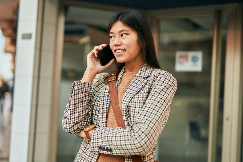 Ung, asiatisk affärskvinna som ler glad med smartphone på stan arkivfoto