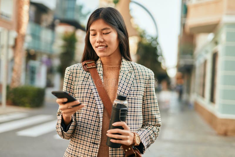 Ung, asiatisk affärskvinna som ler glad med smartphone på stan arkivbilder