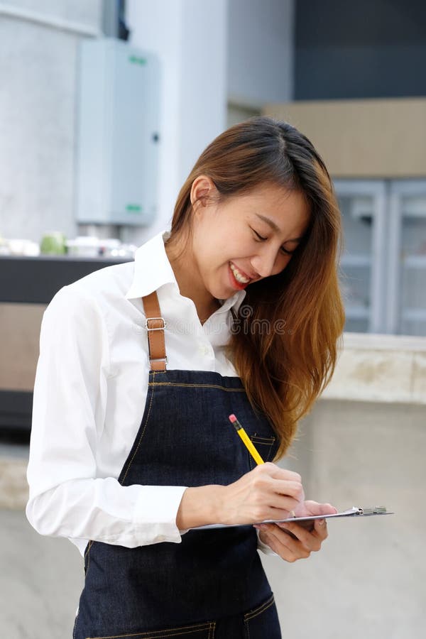 Ung asiatisk barista som tar beställning på kaffekafét med att le fac royaltyfri fotografi Ung asiatisk barista som tar beställning på kaffekafét med att le fac royaltyfri fotografi