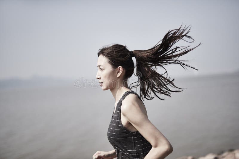 Ung asiatisk kvinna joggar utomhus. Ung asiatisk vuxen kvinna som kör joggande utomhus av havet
