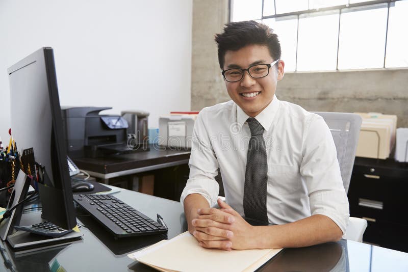 Ung asiatisk manlig professionell på skrivbordet som ler till kameran