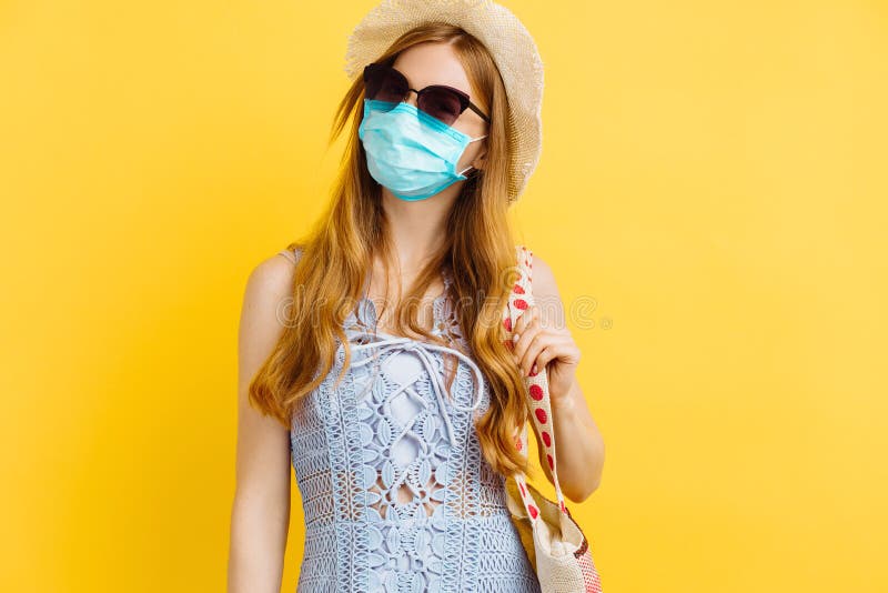 Ung attraktiv kvinna i en mask i en sommarklänning och hatt i gul bakgrund royaltyfri bild