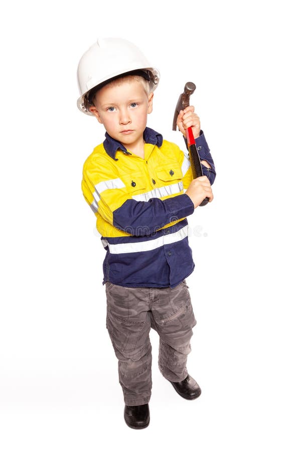 Ung blond caucasian pojkeroll som hi-n?mligen spelar som en byggnadsarbetare i en gul och bl? skjorta, k?ngor, vit h?rd hatt arkivfoto Ung blond caucasian pojkeroll som hi-n?mligen spelar som en byggnadsarbetare i en gul och bl? skjorta, k?ngor, vit h?rd hatt arkivfoto