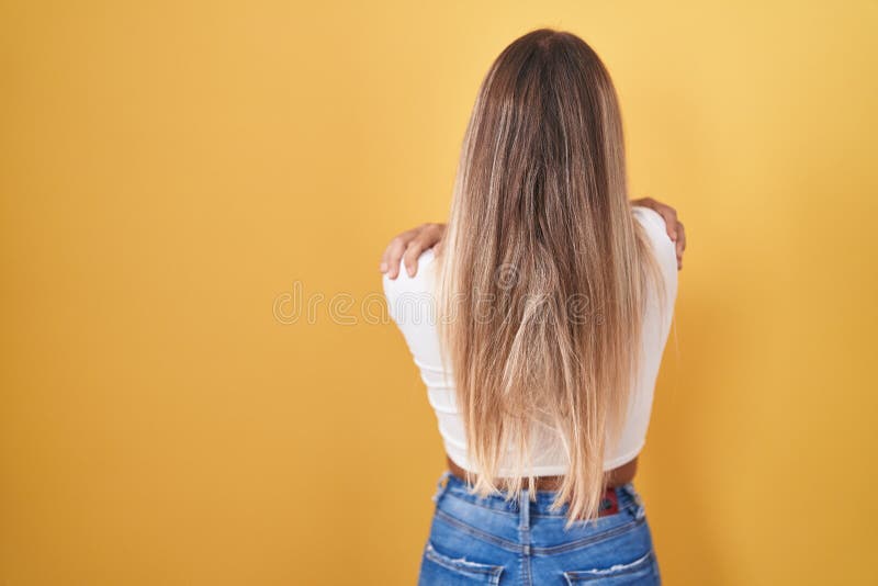Ung, blond kvinna som står över gul bakgrund med hörlurar som kramar sig själv glad och positiv bakifrån arkivbild