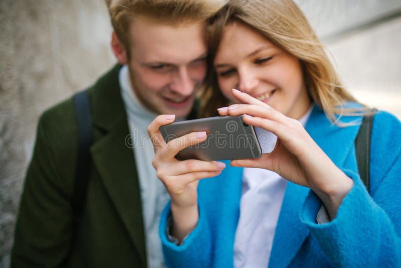 Ung blond man och kvinna som ser på smartphonen och att le royaltyfria bilder Ung blond man och kvinna som ser på smartphonen och att le royaltyfria bilder