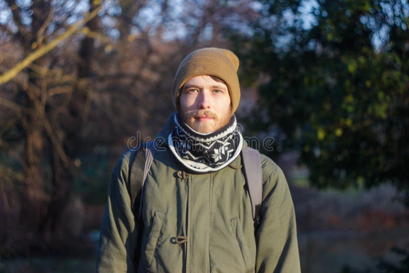 Ung blond vit man med ett skägg som bär en halsduk, en hatt och en ryggsäck royaltyfria foton Ung blond vit man med ett skägg som bär en halsduk, en hatt och en ryggsäck royaltyfria foton