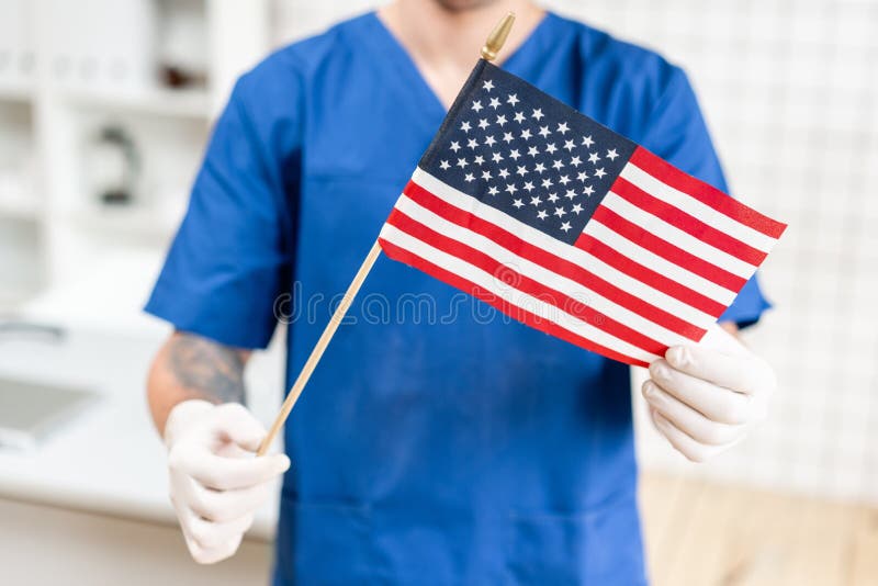 Ung doktorsman som rymmer en amerikanska flaggan i sjukhuset royaltyfri bild Ung doktorsman som rymmer en amerikanska flaggan i sjukhuset royaltyfri bild