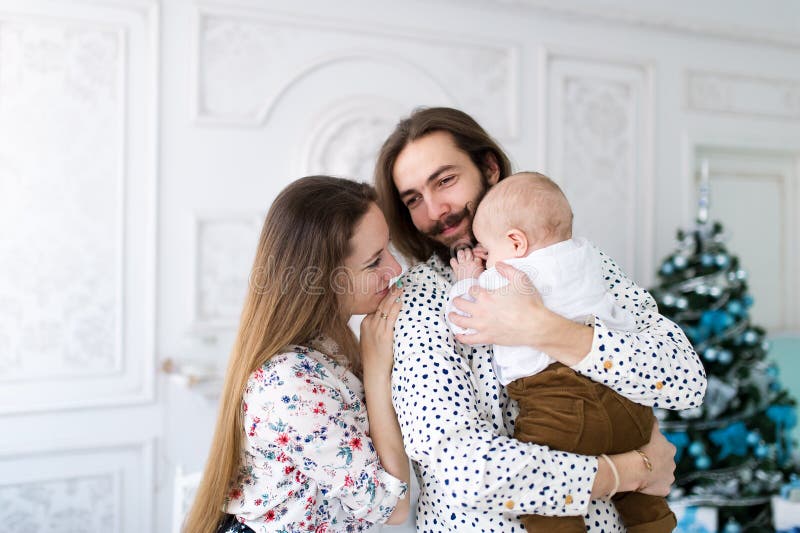 Ung familj av det dela traditionella rånanseendet för julafton tre mot gran-träd royaltyfri fotografi Ung familj av det dela traditionella rånanseendet för julafton tre mot gran-träd royaltyfri fotografi