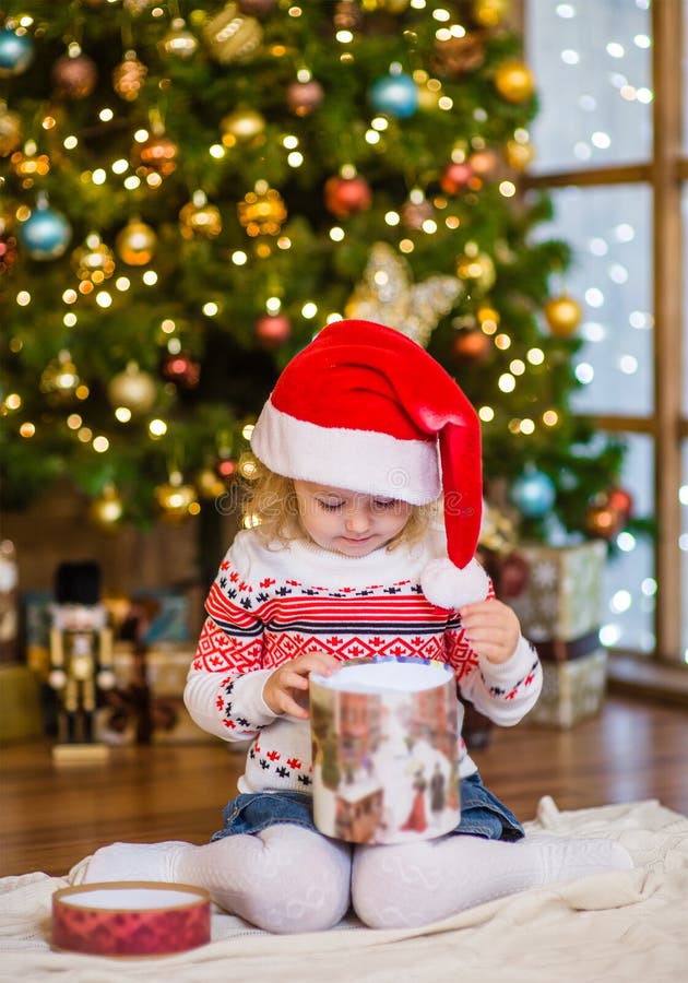 Ung flicka i röda gåvor för jul för santa hattöppning arkivfoto Ung flicka i röda gåvor för jul för santa hattöppning arkivfoto