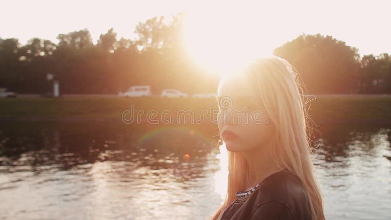 Ung flicka som poserar på grengräset nära floden på solnedgången