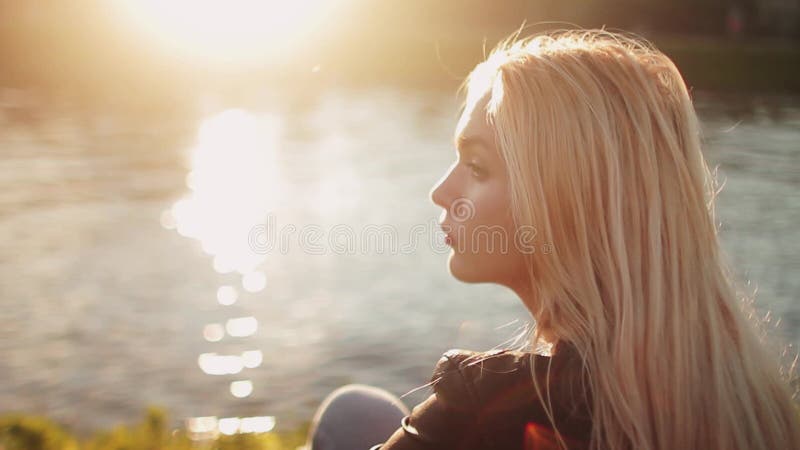 Ung flicka som poserar på grengräset nära floden på solnedgången