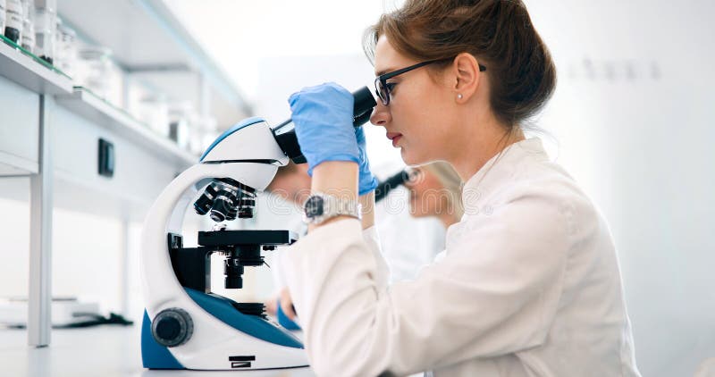 Ung forskare som ser till och med mikroskopet i laboratorium royaltyfri bild