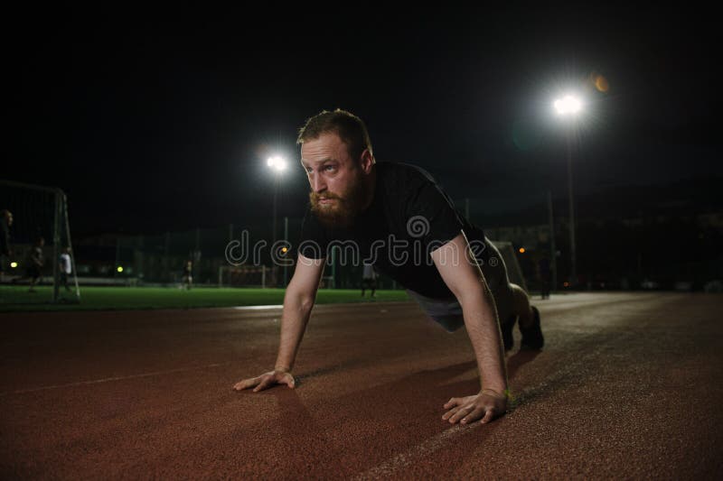 Ung fritidsskvårdad man som driver på Muskulär och stark kille som tränar på nattsport utomhusstadion med ljus arkivbild Ung fritidsskvårdad man som driver på Muskulär och stark kille som tränar på nattsport utomhusstadion med ljus arkivbild