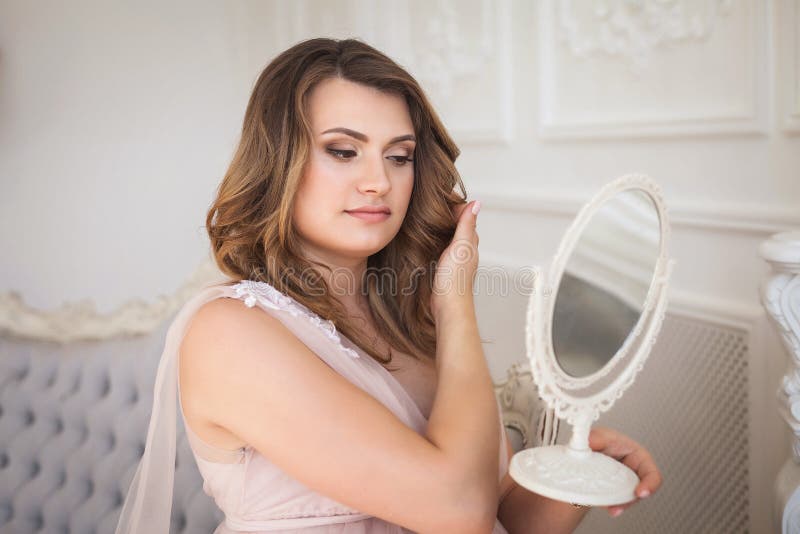 Ung gravid kvinna som beundrar reflexionen i spegeln på soffan i studio royaltyfri bild Ung gravid kvinna som beundrar reflexionen i spegeln på soffan i studio royaltyfri bild