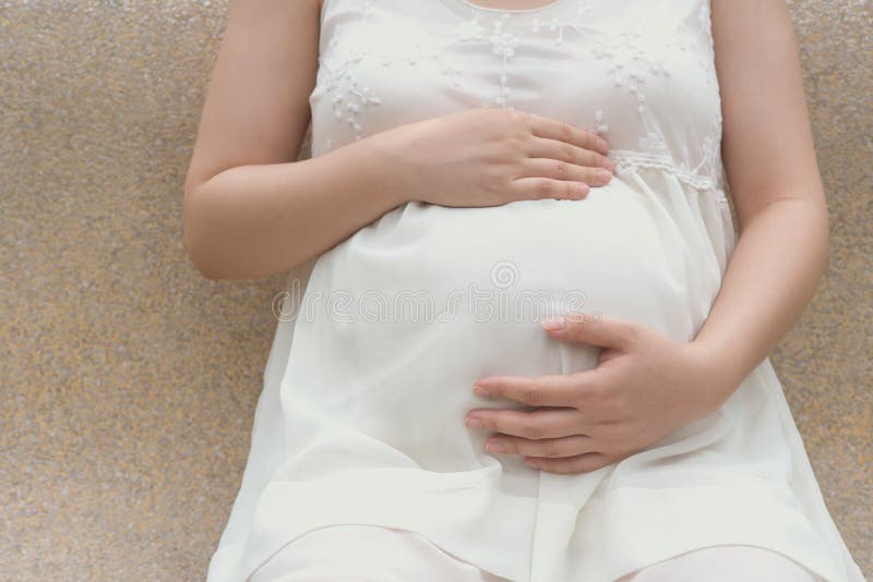 Ung gravid kvinna som sätter händer på buken som känner behandla som ett barn royaltyfria bilder Ung gravid kvinna som sätter händer på buken som känner behandla som ett barn royaltyfria bilder