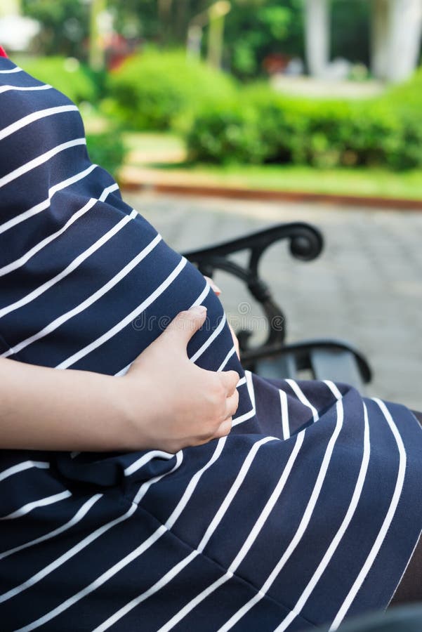 Ung gravid kvinna som sätter händer på buken som känner behandla som ett barn royaltyfria bilder Ung gravid kvinna som sätter händer på buken som känner behandla som ett barn royaltyfria bilder