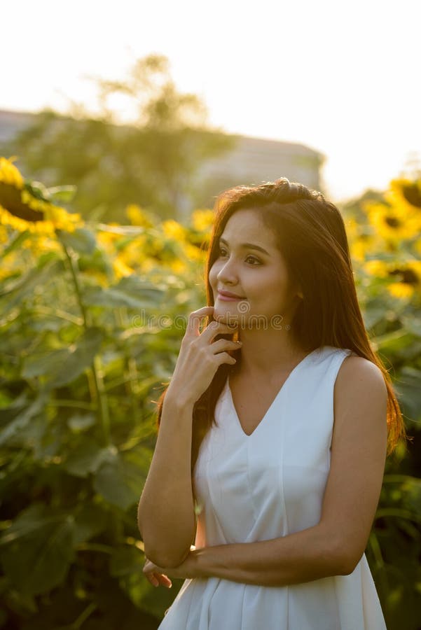 Ung härlig asiatisk kvinna som tänker i fältet av att blomma su arkivbild Ung härlig asiatisk kvinna som tänker i fältet av att blomma su arkivbild