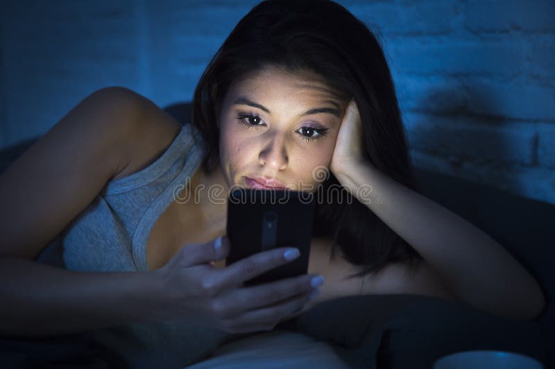 Ung härlig latinsk kvinna på säng sent på natten som smsar genom att använda den trött mobiltelefonen som är sömnig och royaltyfria foton Ung härlig latinsk kvinna på säng sent på natten som smsar genom att använda den trött mobiltelefonen som är sömnig och royaltyfria foton