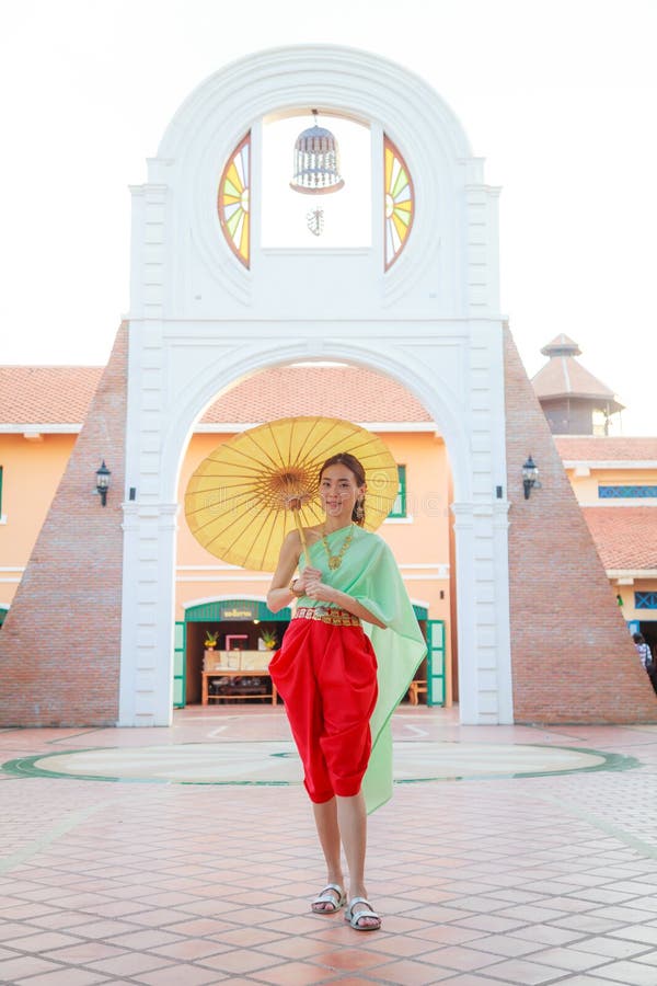 Ung härlig thailändsk asiatisk kvinna i traditionell thailändsk dräkt för tappning med paraplyet i väntan till den välkomna gäste royaltyfri fotografi Ung härlig thailändsk asiatisk kvinna i traditionell thailändsk dräkt för tappning med paraplyet i väntan till den välkomna gäste royaltyfri fotografi