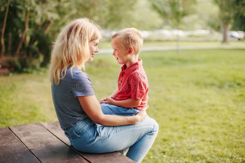 Young Caucasian mother and boy toddler son sitting together face to face. Family mom and child talking communicating outdoor on summer day. Happy authentic family childhood lifestyle. Young Caucasian mother and boy toddler son sitting together face to face. Family mom and child talking communicating outdoor on summer day. Happy authentic family childhood lifestyle