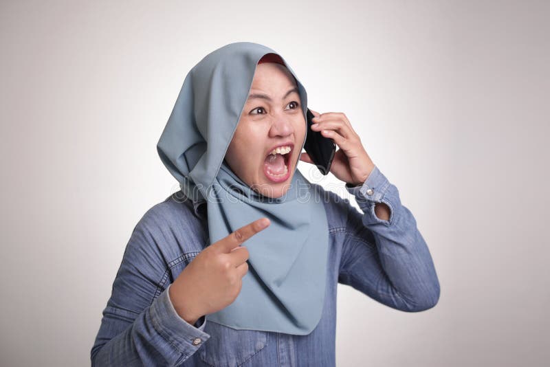 Young Asian muslim woman angry by phone call, screaming on her phone. Close up body portrait isolated on white. Young Asian muslim woman angry by phone call, screaming on her phone. Close up body portrait isolated on white