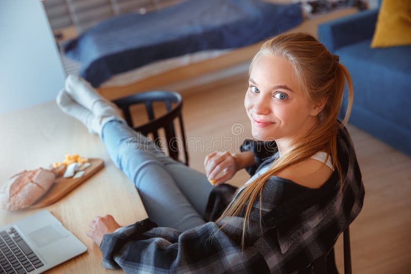 Ung kvinna hemma i köket som äter och använder bärbara datorn arkivfoton Ung kvinna hemma i köket som äter och använder bärbara datorn arkivfoton