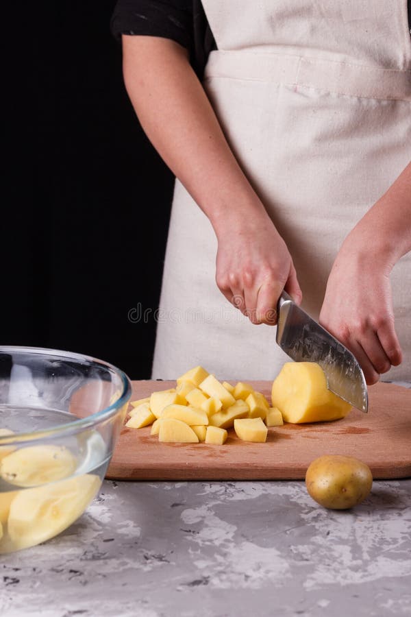 Ung kvinna i en apron skär potatis royaltyfria foton