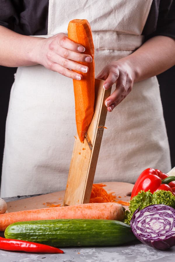 Ung kvinna i en grå apron skär morötter arkivfoto