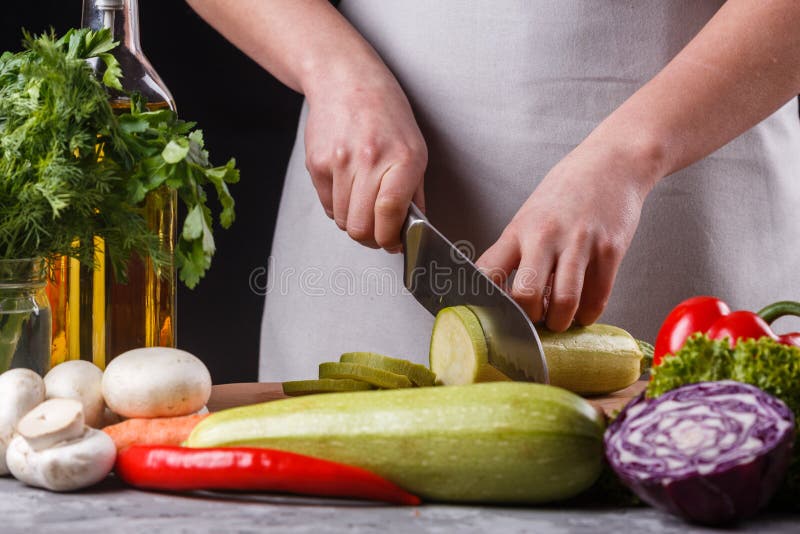 Ung kvinna i en grå apron skär en zucchini arkivbild