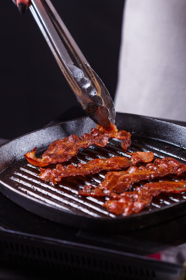 Ung kvinna i en grå aprons bacon arkivbild