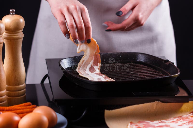 Ung kvinna i en grå aprons bacon royaltyfri bild