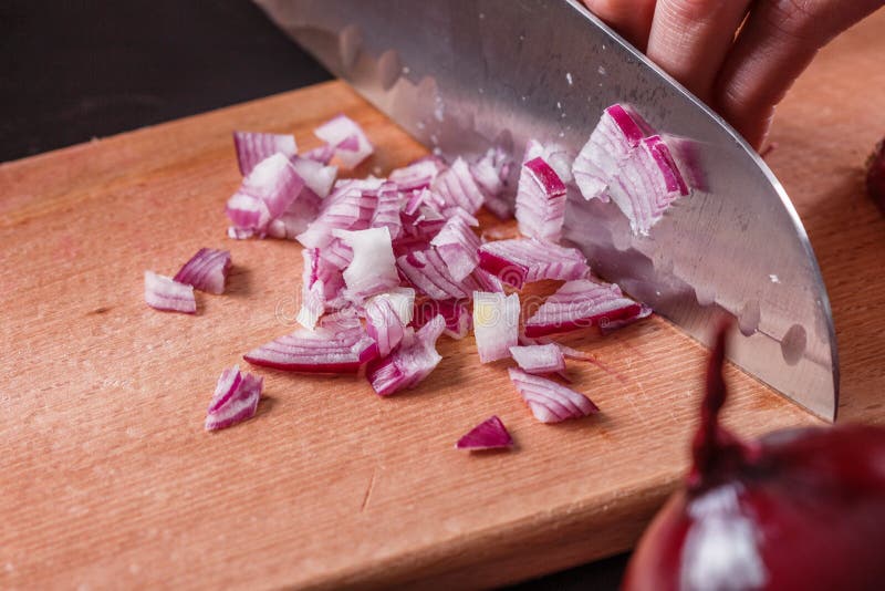 Ung kvinna i en grå aprons skär ner den röda löken arkivfoto